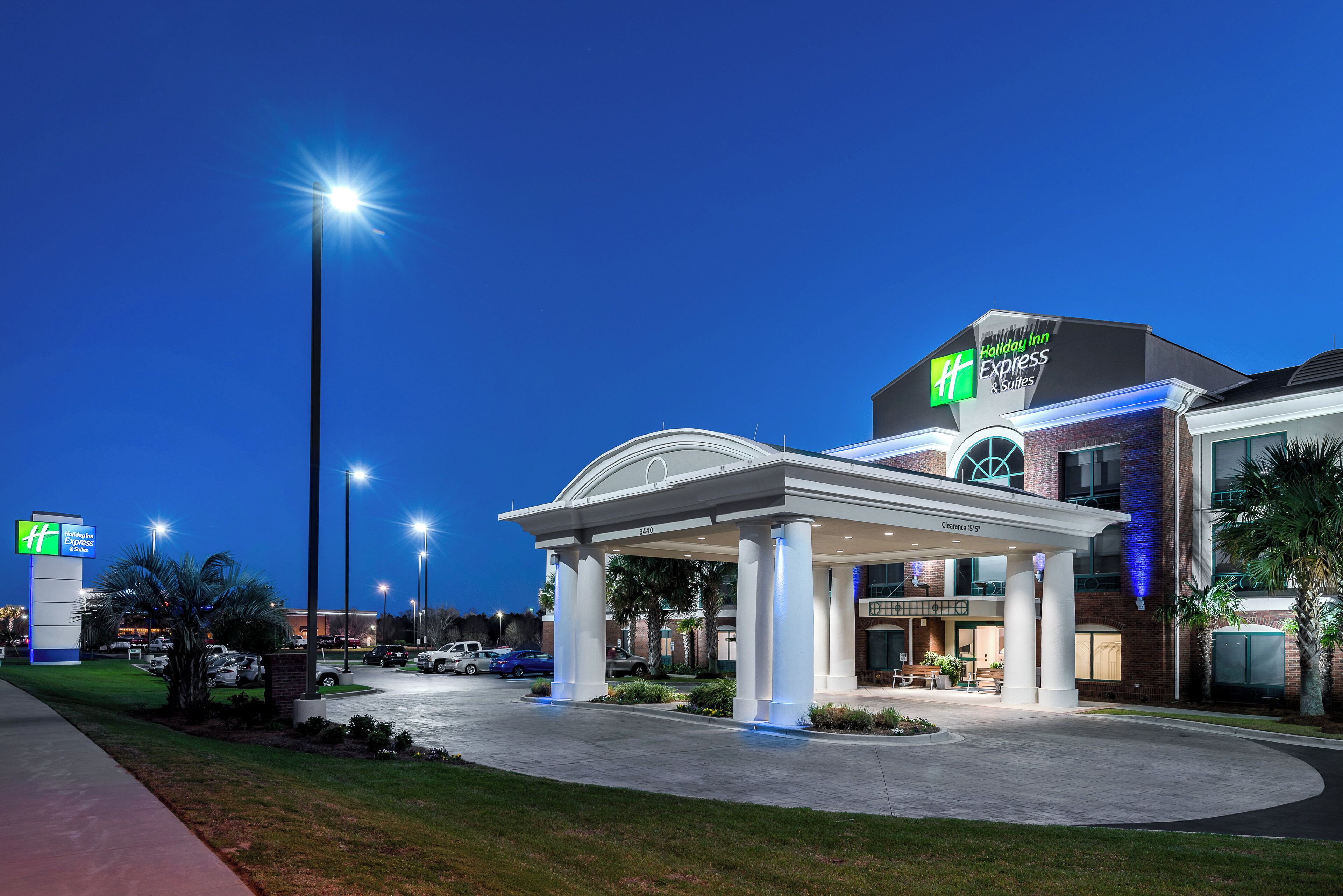 A Holiday Inn Express & Suites with a covered entrance, parking area, and a clear sky.