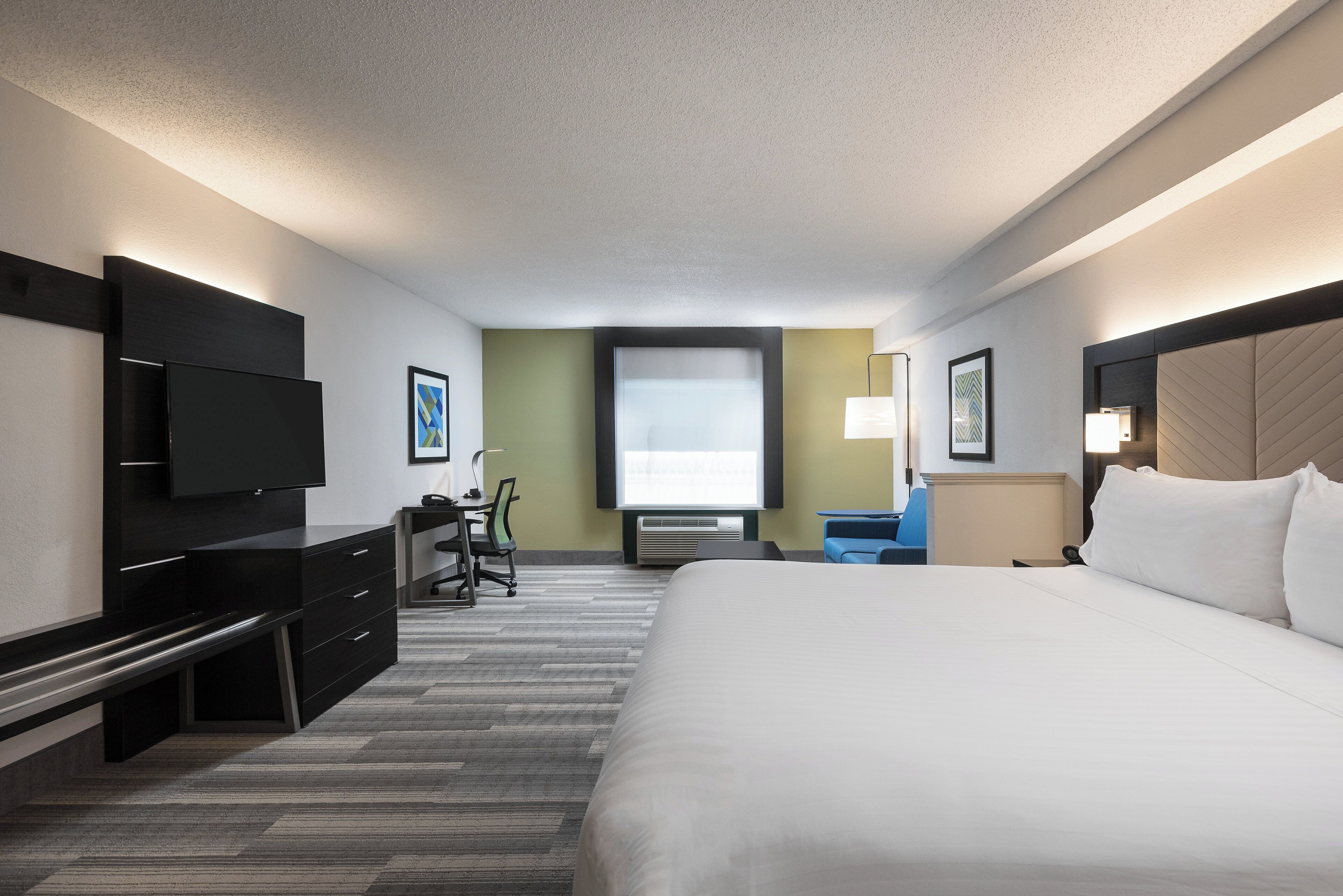 A hotel room with a large bed, a desk with a chair, a television, and a window.