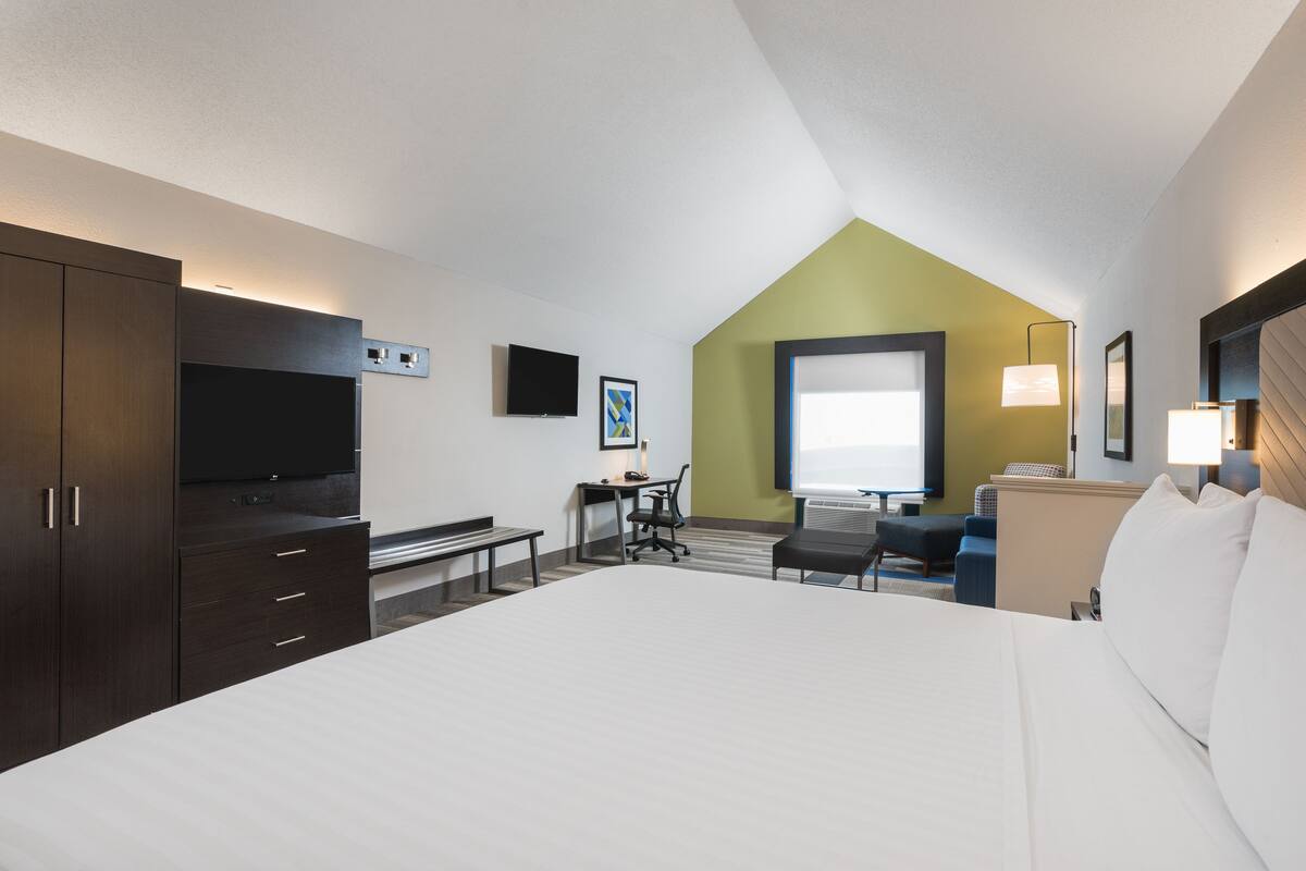 Habitación de hotel con una cama grande, un escritorio con silla, televisión y ventana con vistas.