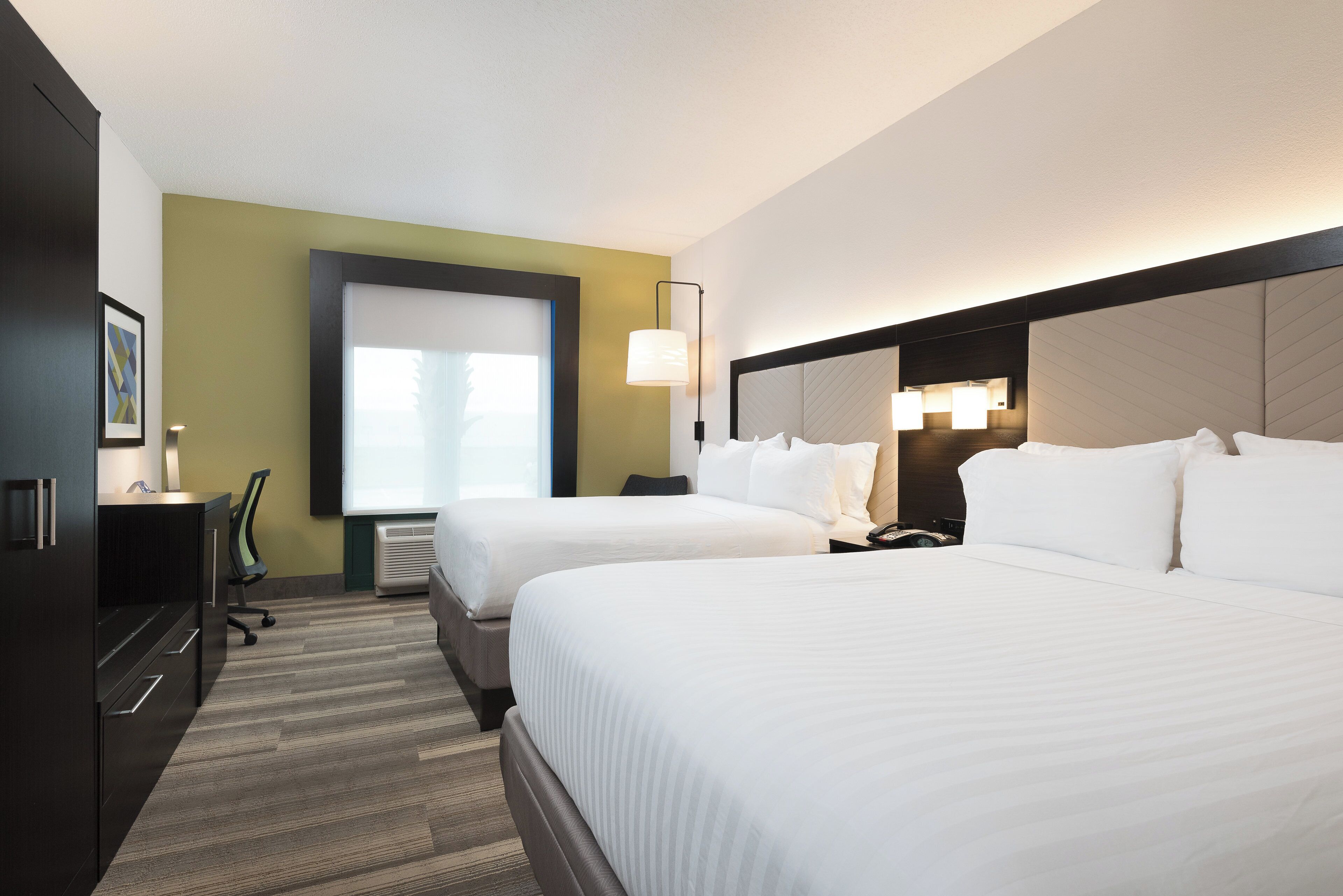 A hotel room with two beds, a desk, a chair, a lamp, and a window.