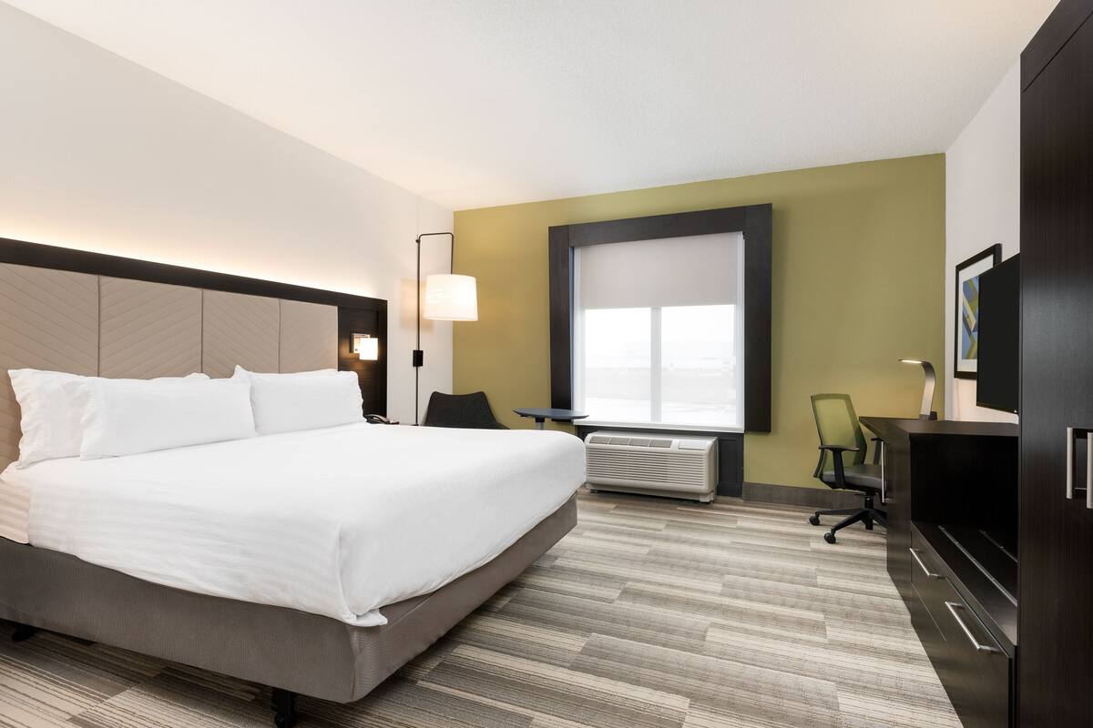 Una habitación de hotel con una cama grande, un escritorio, aire acondicionado y televisión.