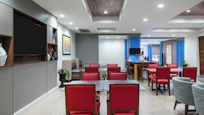 Un restaurante moderno con sillas tapizadas en rojo, un televisor de pantalla plana montado en la pared e iluminación empotrada en el techo.