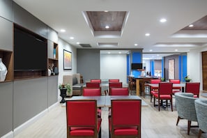 A modern restaurant with red upholstered chairs, a flat-screen TV mounted on the wall, and a ceiling with recessed lighting. - Holiday Inn Express & Suites Florence I-95 & I-20 Civic Ctr by IHG (Florence)