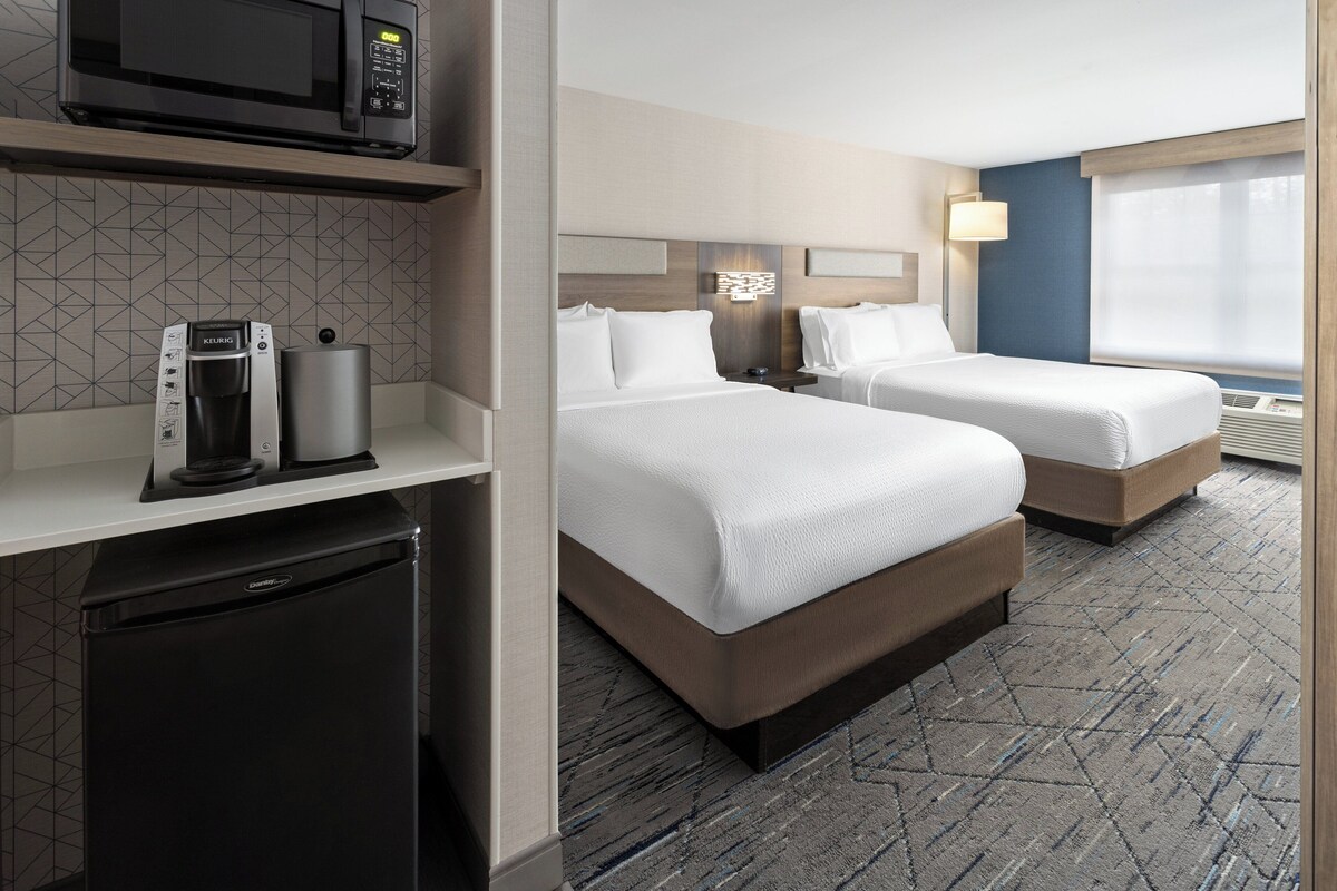 A hotel room with two beds, a minibar, a coffee maker, and a microwave.