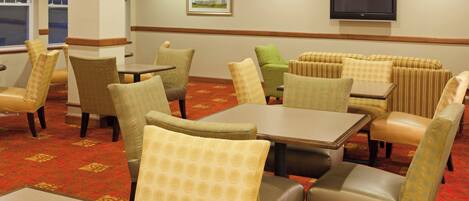 A hotel dining area with tables and chairs, a television on the wall, and a painting.