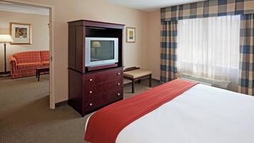 Une chambre d’hôtel avec un lit, un téléviseur posé sur une commode en bois, une chaise, un bureau et une fenêtre avec des rideaux.