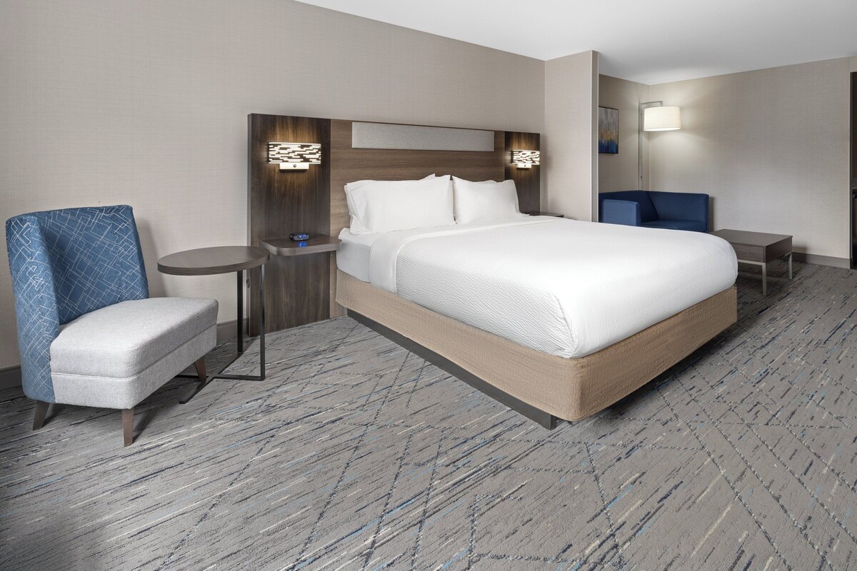 A hotel room with a large bed, a small round table, a blue chair, and a nightstand.