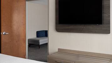 A hotel room with a bed, a TV mounted on the wall, a wooden dresser, and a door leading to another room.