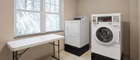 Een wasserette met een wasmachine, droger en een tafel.