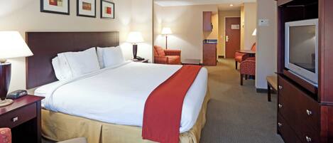 A hotel room with a large bed, a desk, a chair, a television, and a small kitchenette.