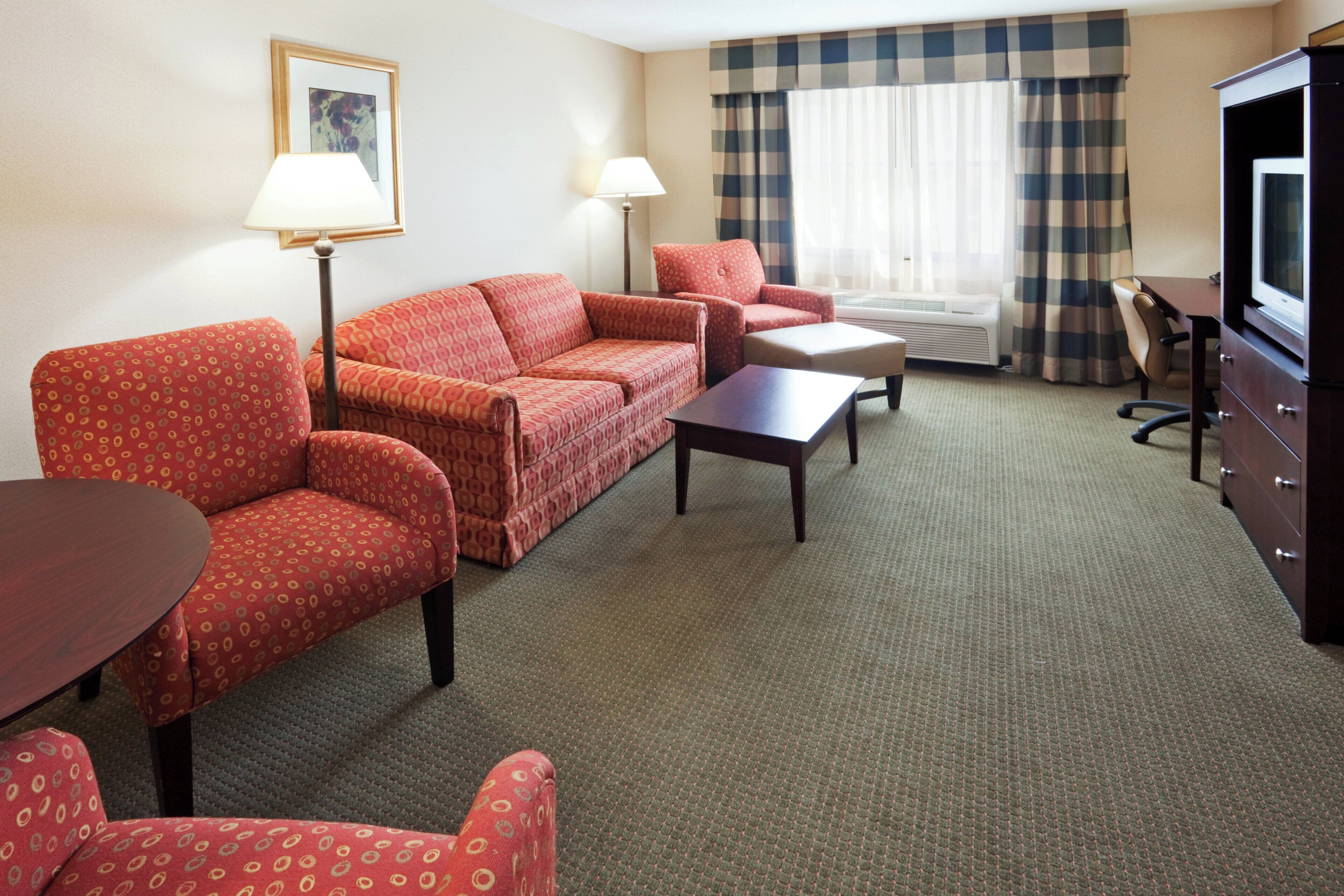 Een hotelkamer met een zithoek, een klein tafeltje, een televisie en een raam met gordijnen.