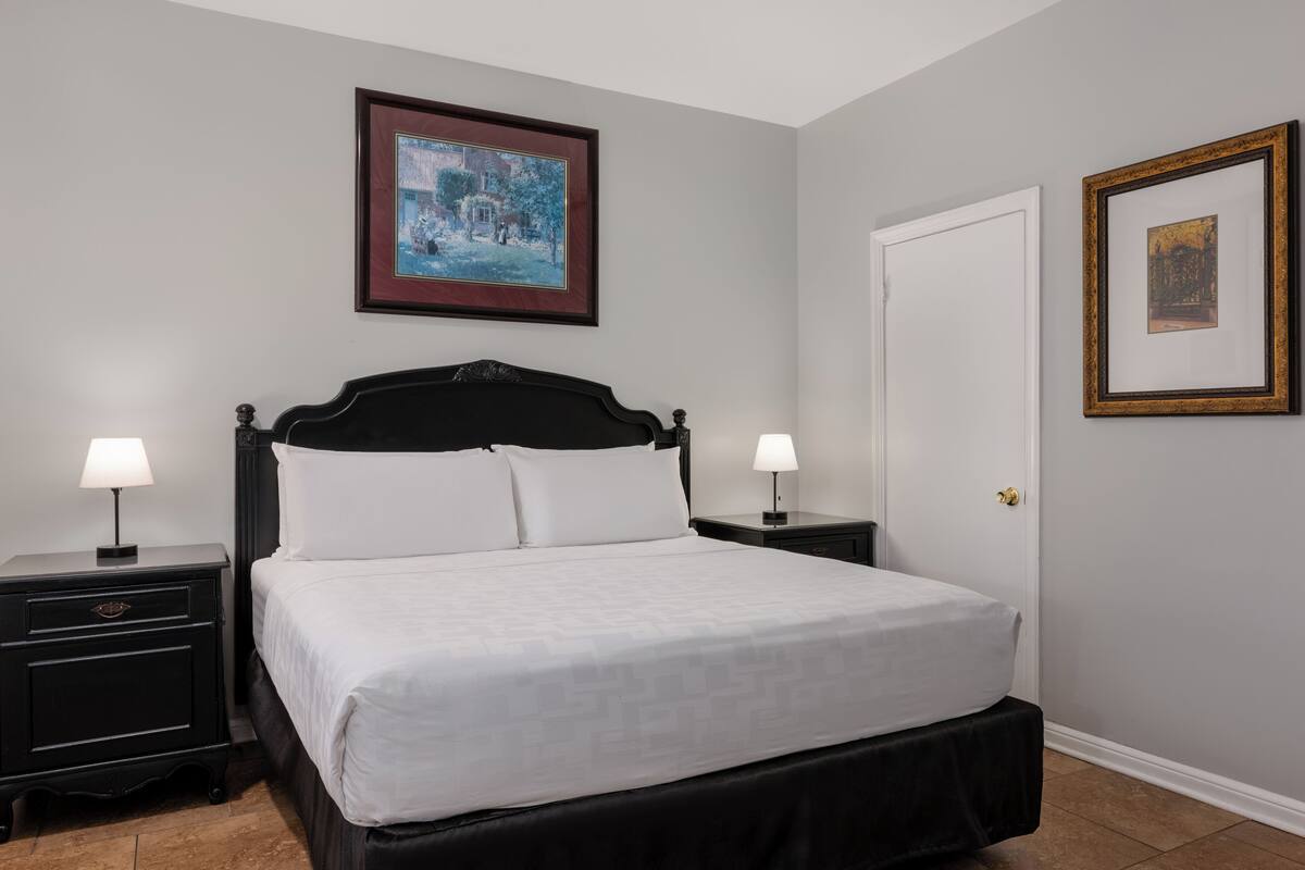 A neatly made bed with white linens, two bedside tables with lamps, and two framed pictures on the walls.