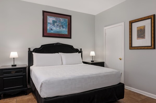 A neatly made bed with white linens, two bedside tables with lamps, and two framed pictures on the walls.
