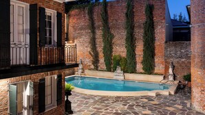 A swimming pool with stone tiles, surrounded by brick walls and a balcony with black shutters. - Chateau Hotel (New Orleans)