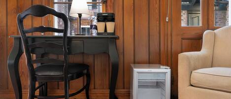 Una habitación con pared de paneles de madera, una silla negra, una mesita blanca con una lámpara y un sofá color beige.