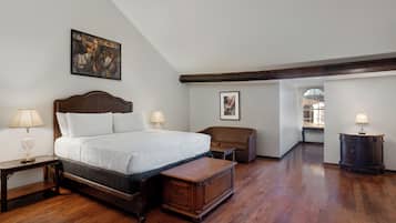 A bedroom with a large bed, a wooden nightstand, a bench, a dresser, and a painting on the wall.
