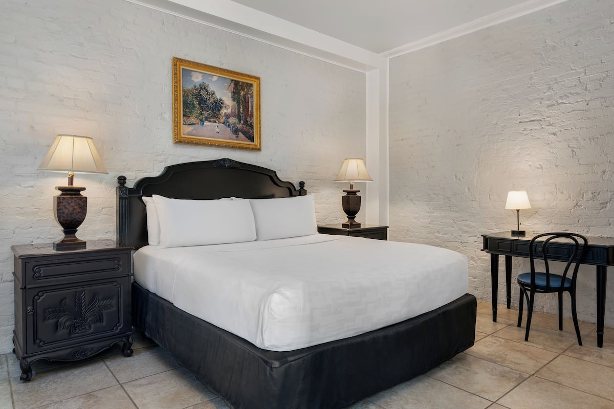A bedroom with a large bed, two bedside tables with lamps, a desk with a chair, and a painting on the wall.