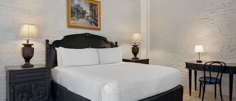 A bedroom with a large bed, two bedside tables with lamps, a desk with a chair, and a painting on the wall.