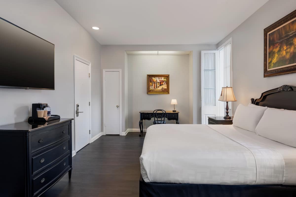 A hotel room with a large bed, a desk with a chair, a flat-screen TV, and a painting on the wall.