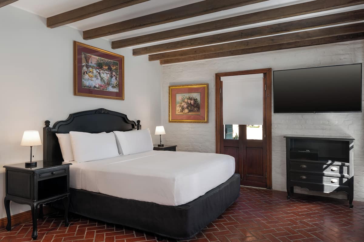 A bedroom with a large bed, two bedside tables with lamps, a flat-screen TV mounted on the wall, and a wooden dresser.