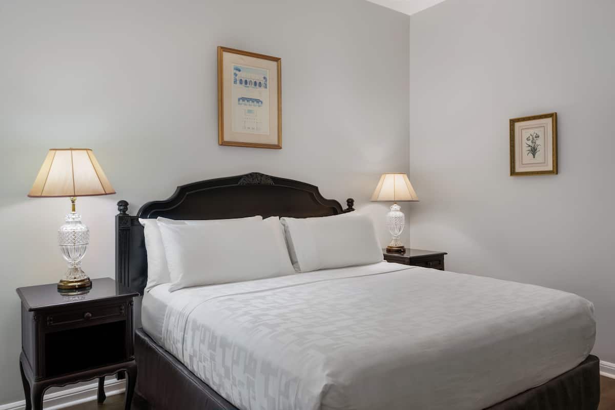 A neatly made bed with white linens, two bedside tables with lamps, and framed pictures on the walls.