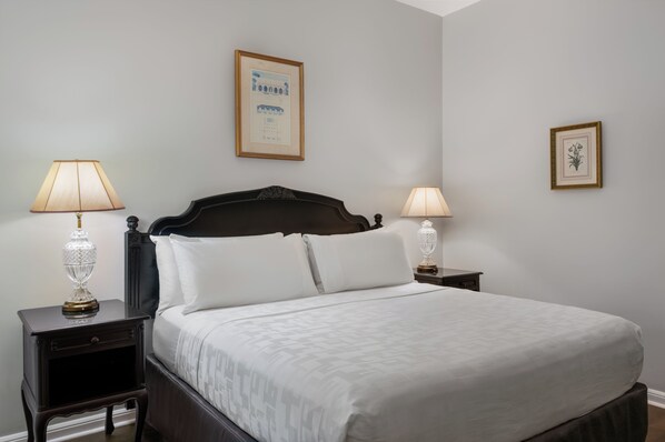 A neatly made bed with white linens, two bedside tables with lamps, and framed pictures on the walls.