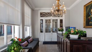 A spacious room with a large window, a dark wood cabinet, a bench with cushions, and a chandelier. - Chateau Hotel (New Orleans)