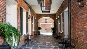 A covered outdoor patio with stone flooring, brick walls, and metal furniture. - Chateau Hotel (New Orleans)
