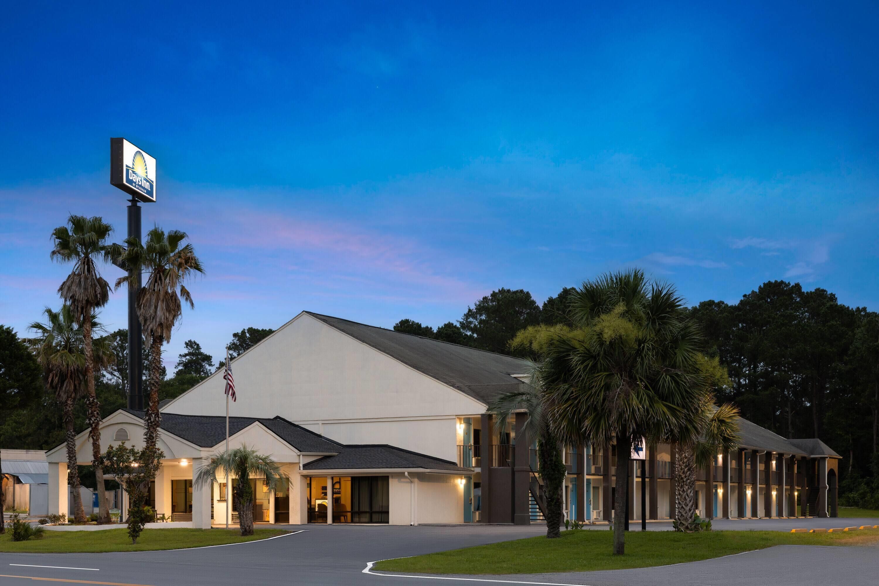 A motel with a large sign, multiple rooms, and a parking area.