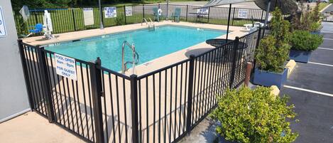 A swimming pool with a black fence, surrounded by potted plants and a parking lot.