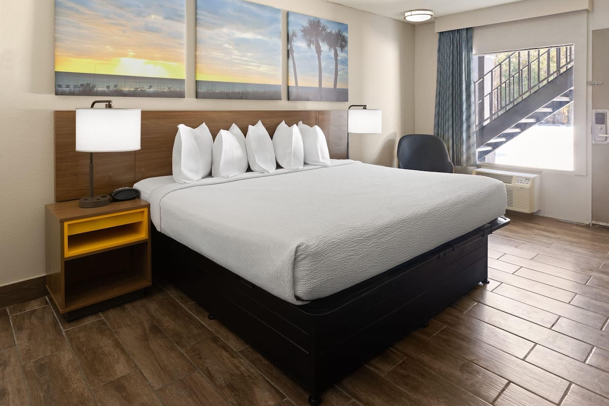 A hotel room with a large bed, two bedside lamps, a nightstand, a chair, and a view of a staircase and outdoor area.
