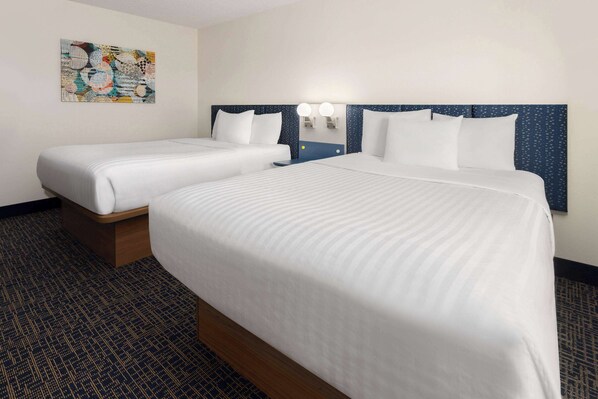 A hotel room with two beds, a nightstand with a lamp, and a wall-mounted artwork.