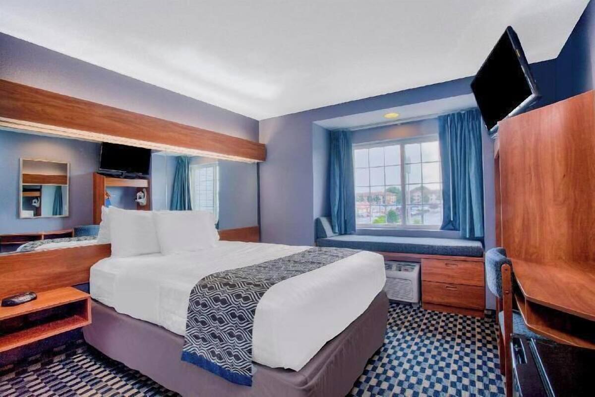 A hotel room with a bed, a desk, a chair, a TV, and a window with curtains.