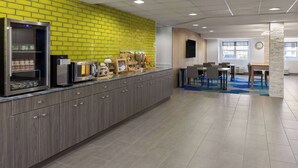 A modern kitchen area with a yellow brick wall, stainless steel appliances, and a seating area with tables and chairs. - Microtel Inn & Suites by Wyndham Dover (Dover)