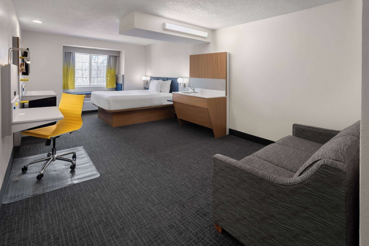 A hotel room with a bed, a desk, a chair, a sofa, and a bathroom area.