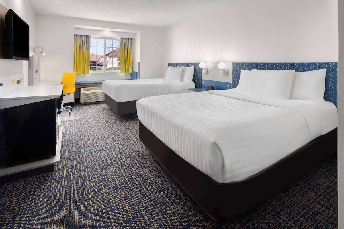 A hotel room with two beds, a desk, a chair, and a TV.