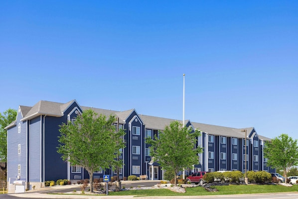 A multi-story hotel with a blue exterior, a flagpole, and a parking lot with several cars.