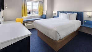 A hotel room with a large bed, a desk, a window with yellow curtains, and a view of the outside. - Microtel Inn & Suites by Wyndham Dover (Dover)