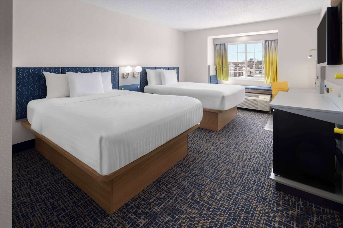 A hotel room with two beds, a desk, a TV, and a window with curtains.
