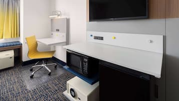 A hotel room with a desk, a chair, a microwave, a TV, and a small cabinet.