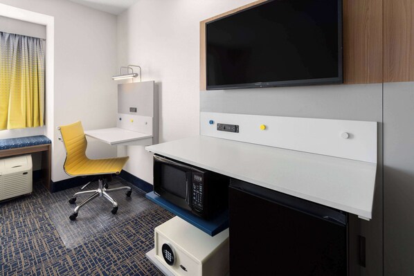 A hotel room with a desk, a chair, a microwave, a TV, and a small cabinet.