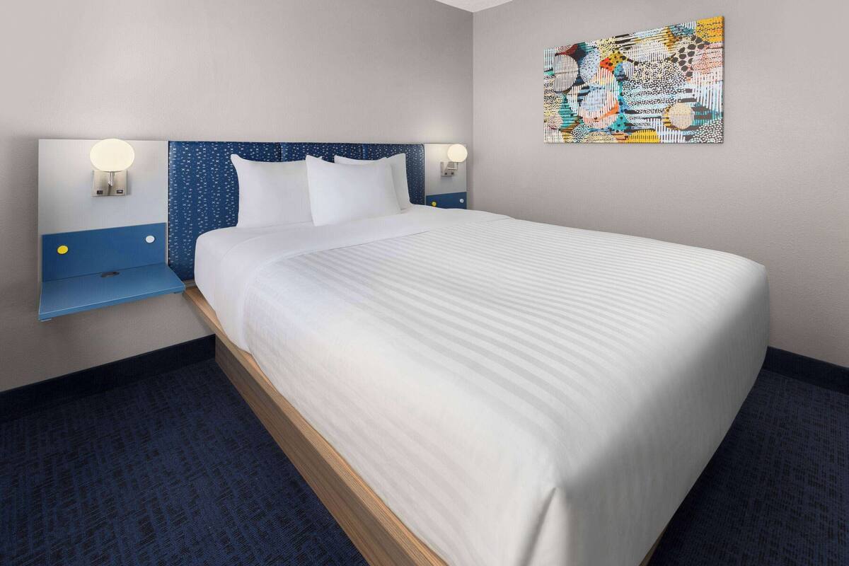 A neatly made bed with a blue headboard and two bedside lamps.