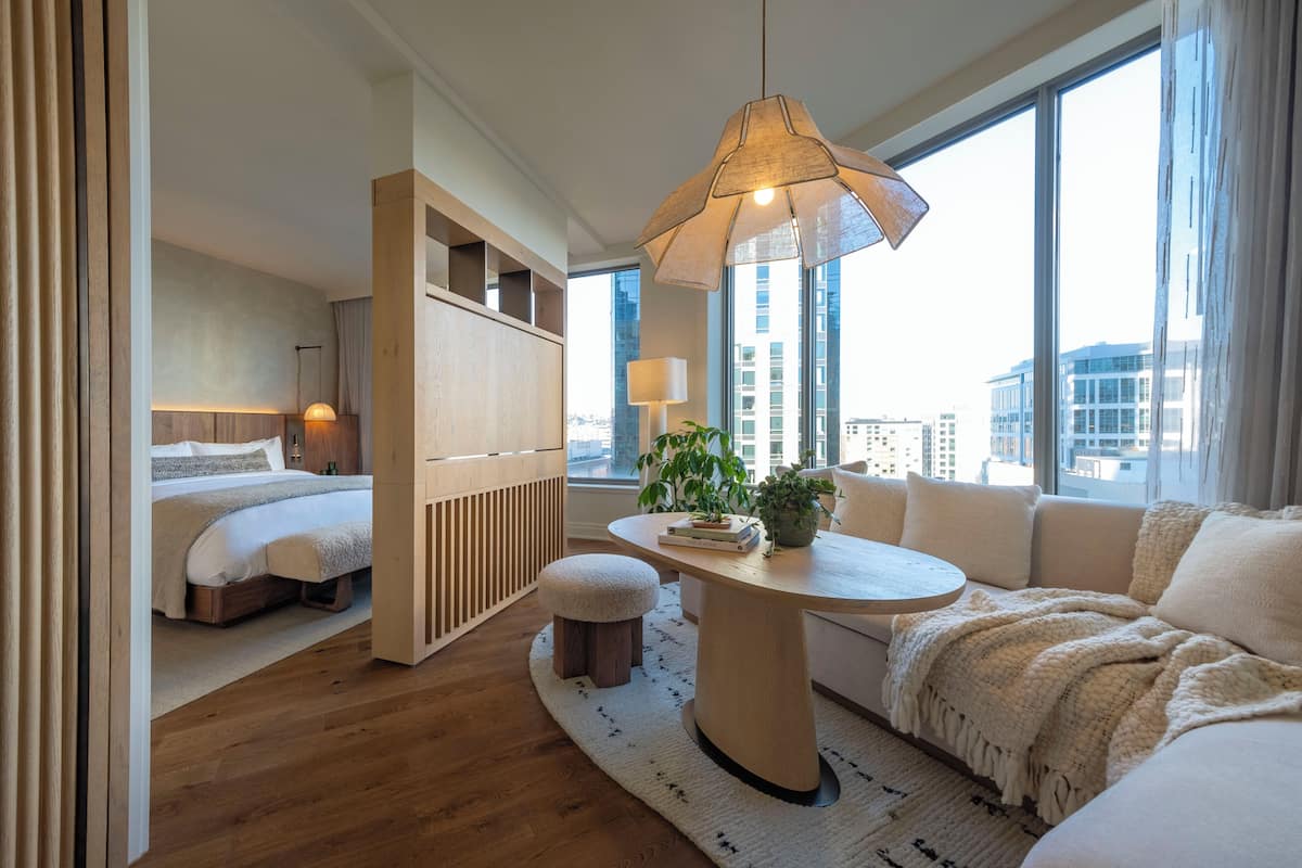 A modern hotel room with a large window, a round table, a sofa, and a bed.