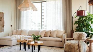Ein modernes Wohnzimmer mit einer Couch, einem Couchtisch, einem Sessel und einem großen Fenster mit Vorhängen.