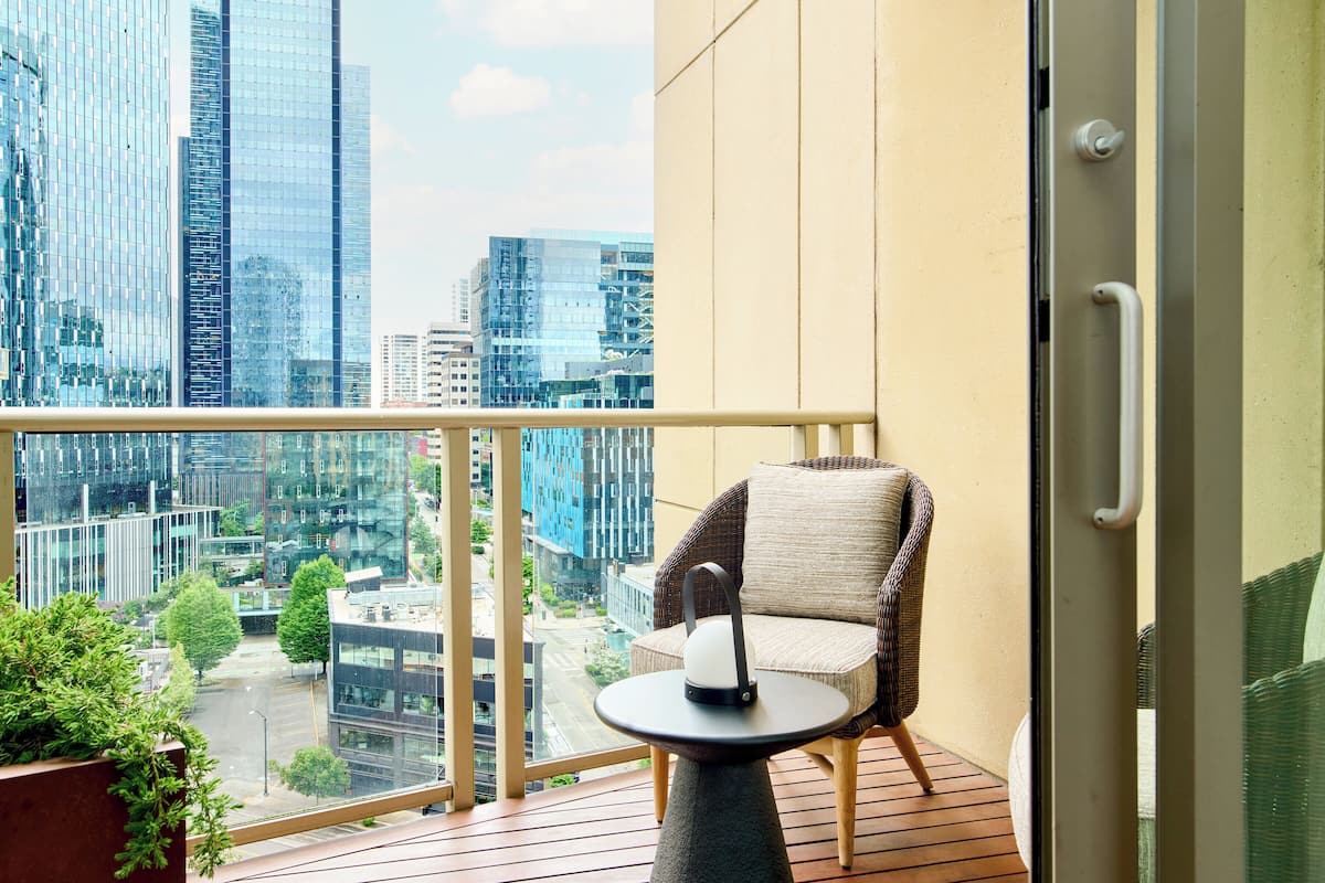 A balcony with a wicker chair, a small table, and a view of city buildings.