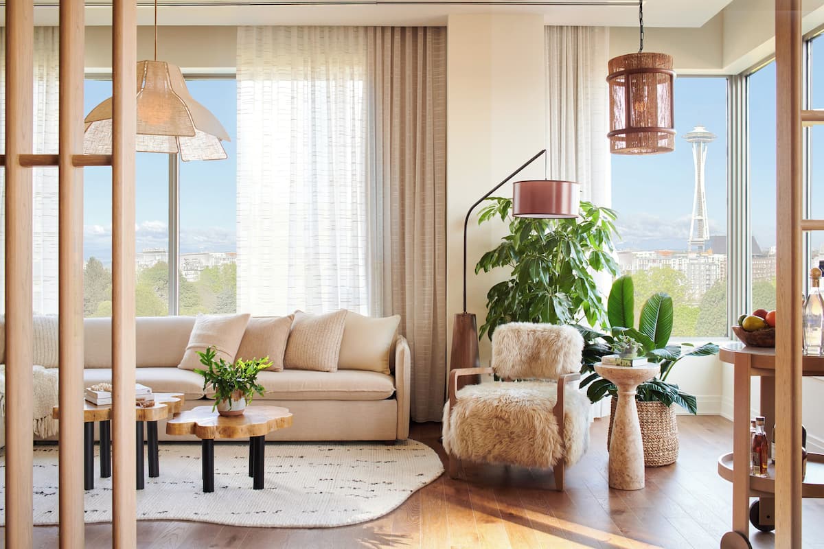 A modern living room with a sofa, armchair, and coffee table, large windows with a view of a tower, and various plants.