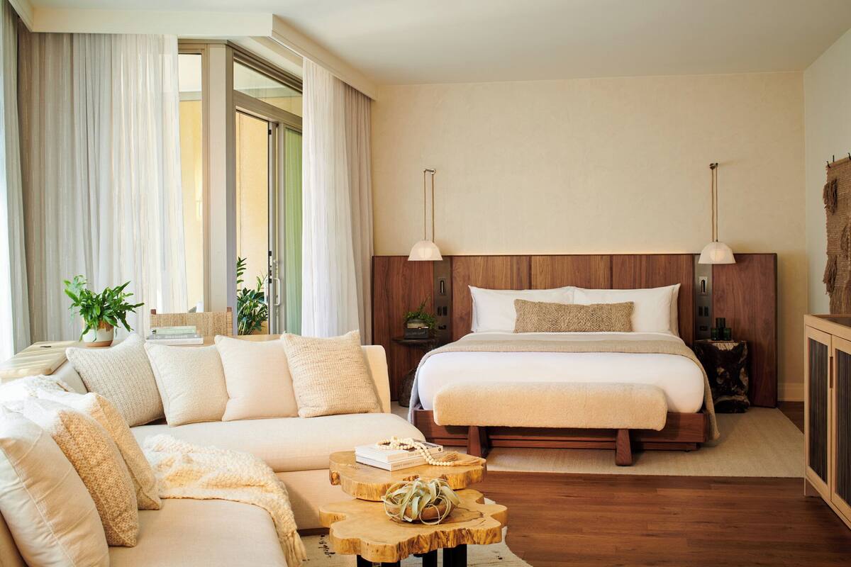 A modern bedroom with a large bed, a sofa, a wooden coffee table, and a view of the outdoors.