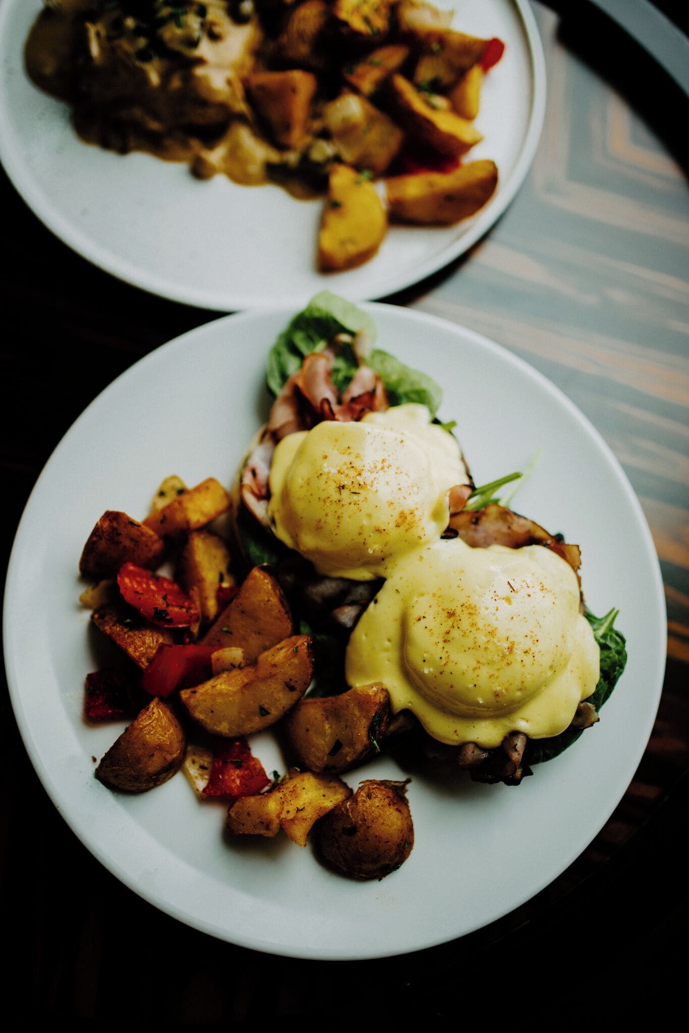 Dos platos de comida, uno con huevos benedictinos y otro con patatas y verduras.