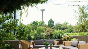 An outdoor seating area with wicker furniture, a round table, and potted plants. - 1 Hotel Seattle (Seattle)