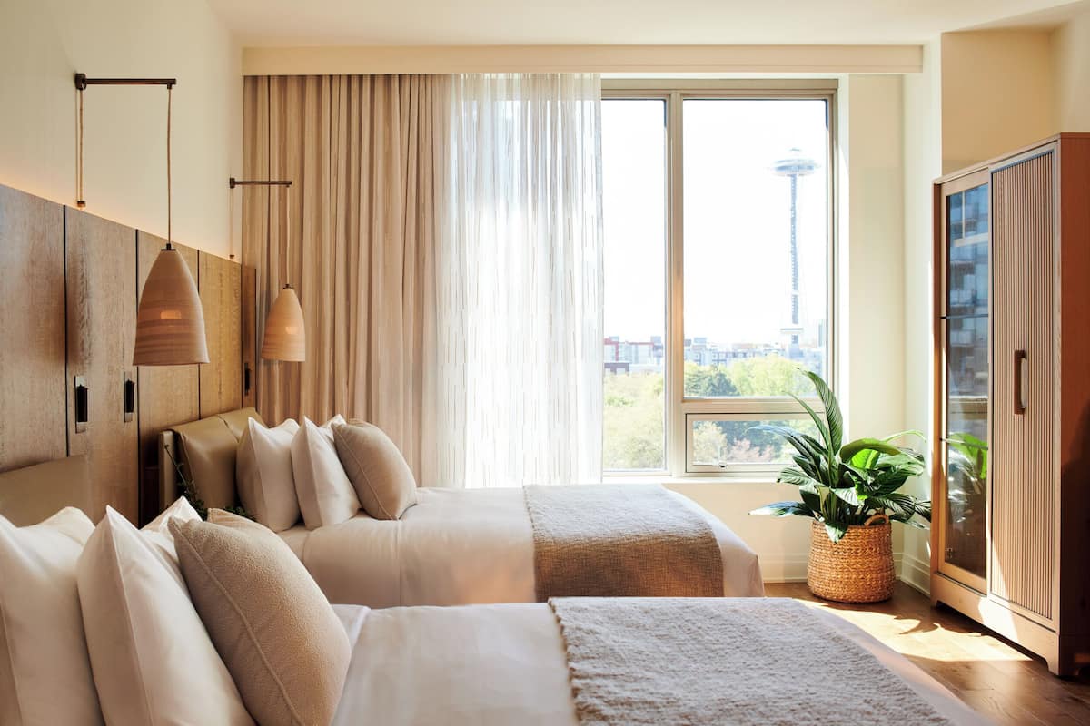 A hotel room with two beds, a large window with a view of a tower, a wardrobe, and a potted plant.